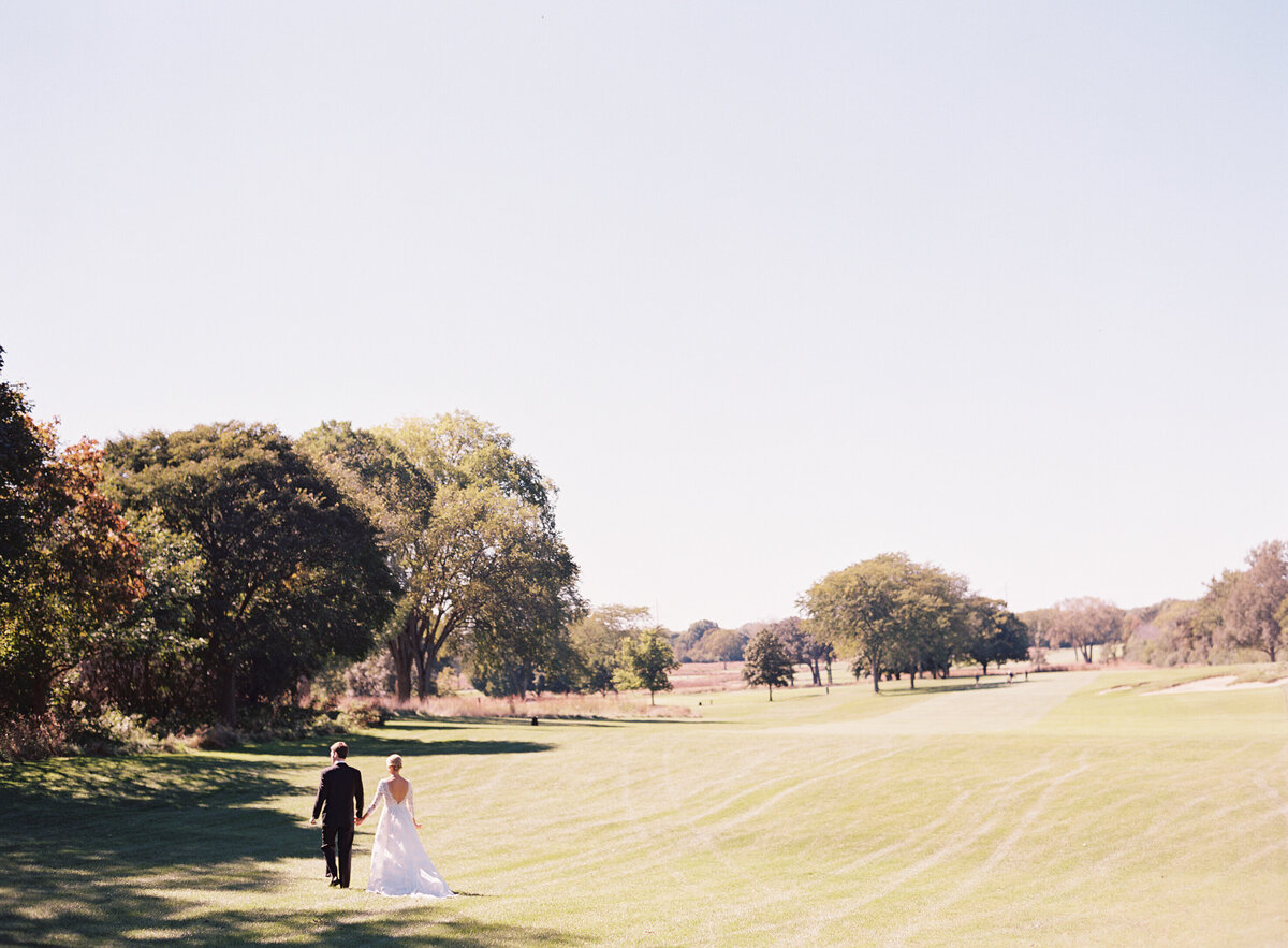 The bride and groom holding hands walking on the grounds at the Onwentsia country club.