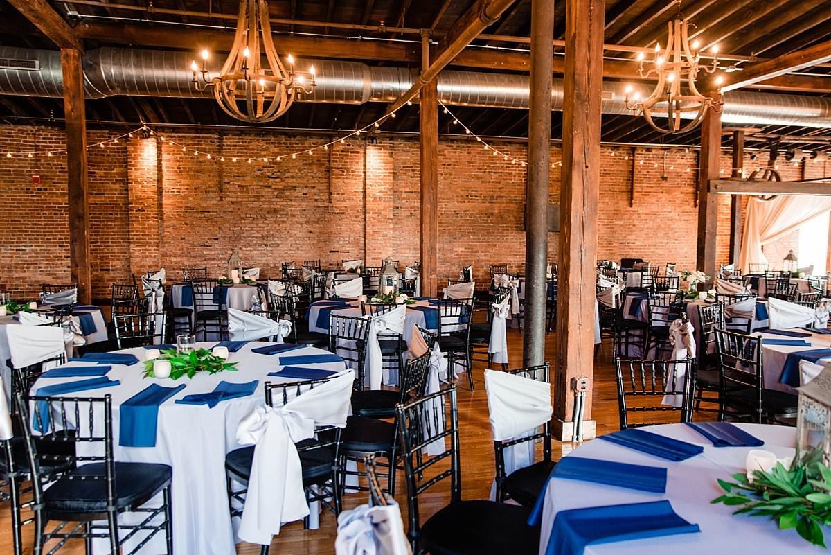 Round tables set for Cannery ONE wedding reception featuring black chivari chairs and soft blues and greenery throughout