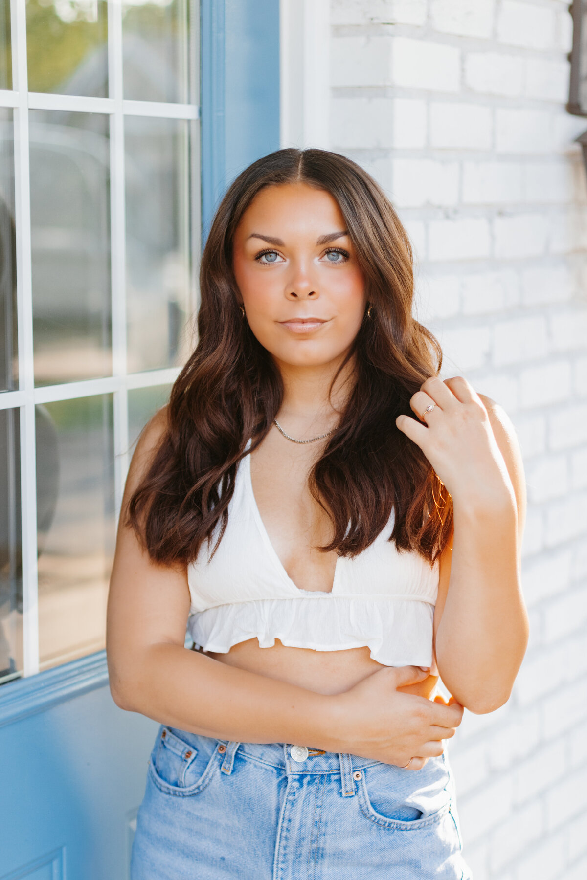 Senior girl in a white top and jeans posing in front of a white wall and blue door