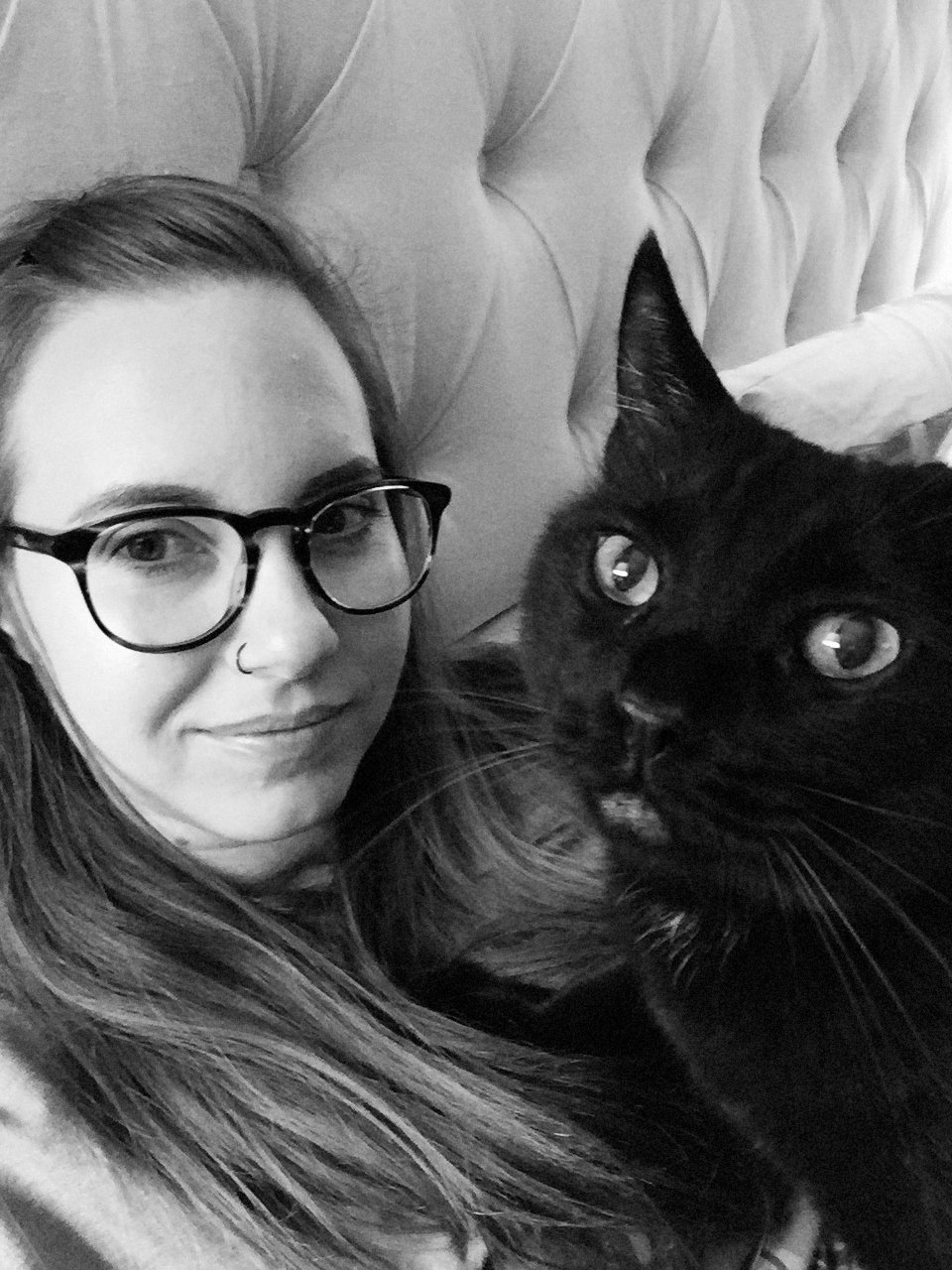 A girl poses with her black cat both looking at camera