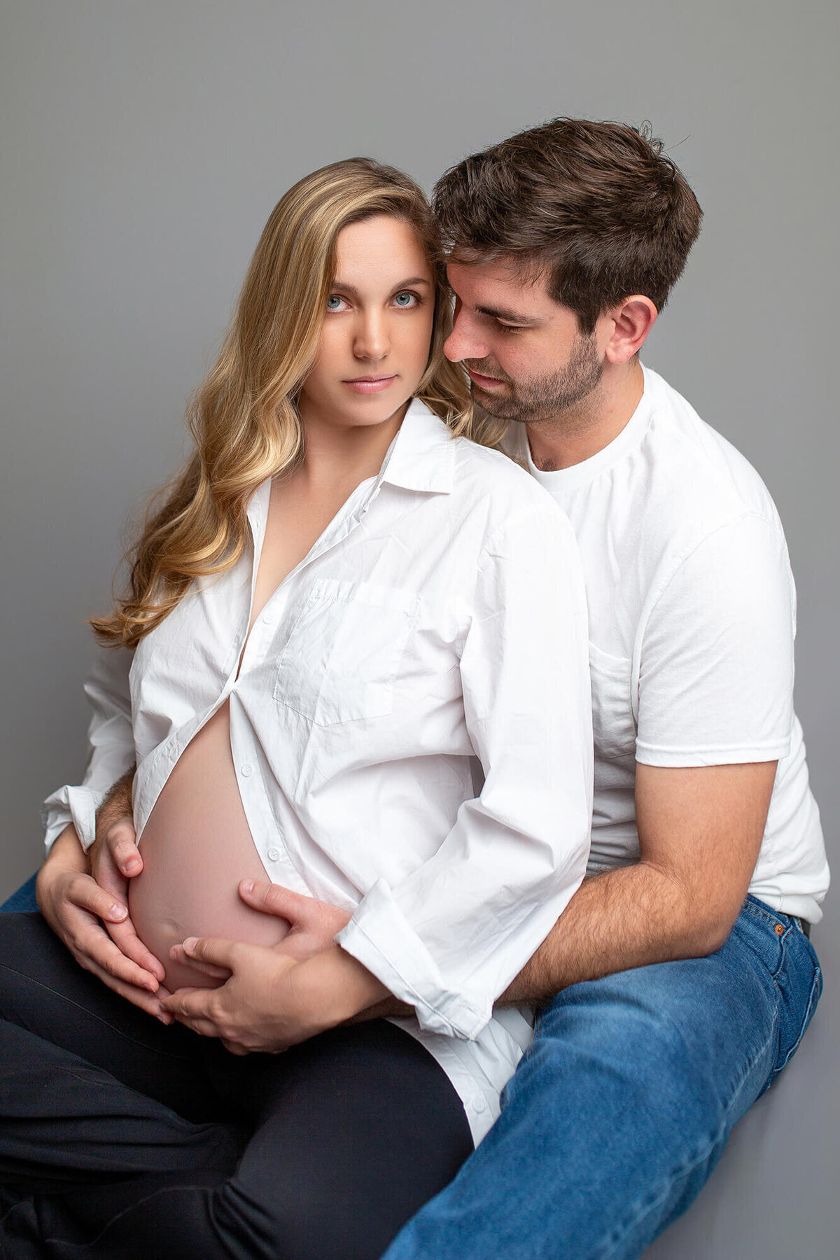 Neutral toned maternity studio session. Dad and holding moms belly from behind.