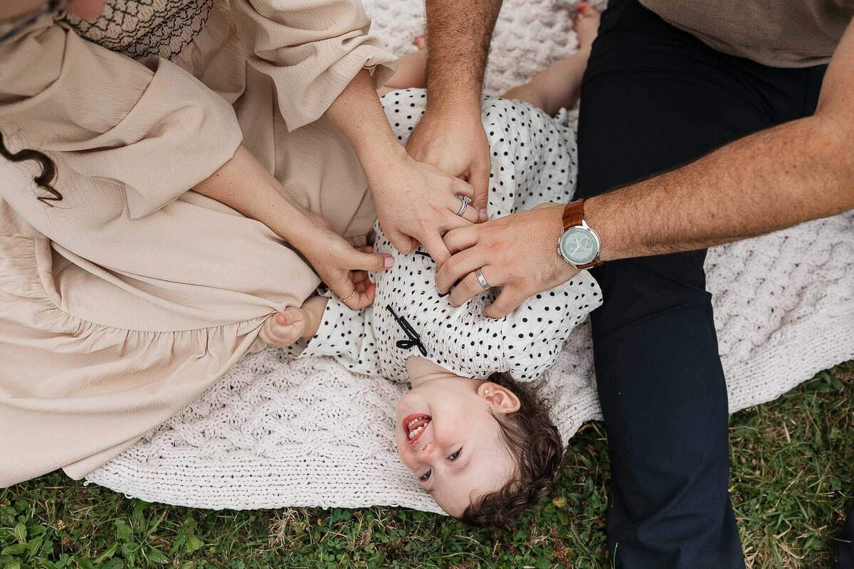 Parents tickling daughter on blanket in field.
