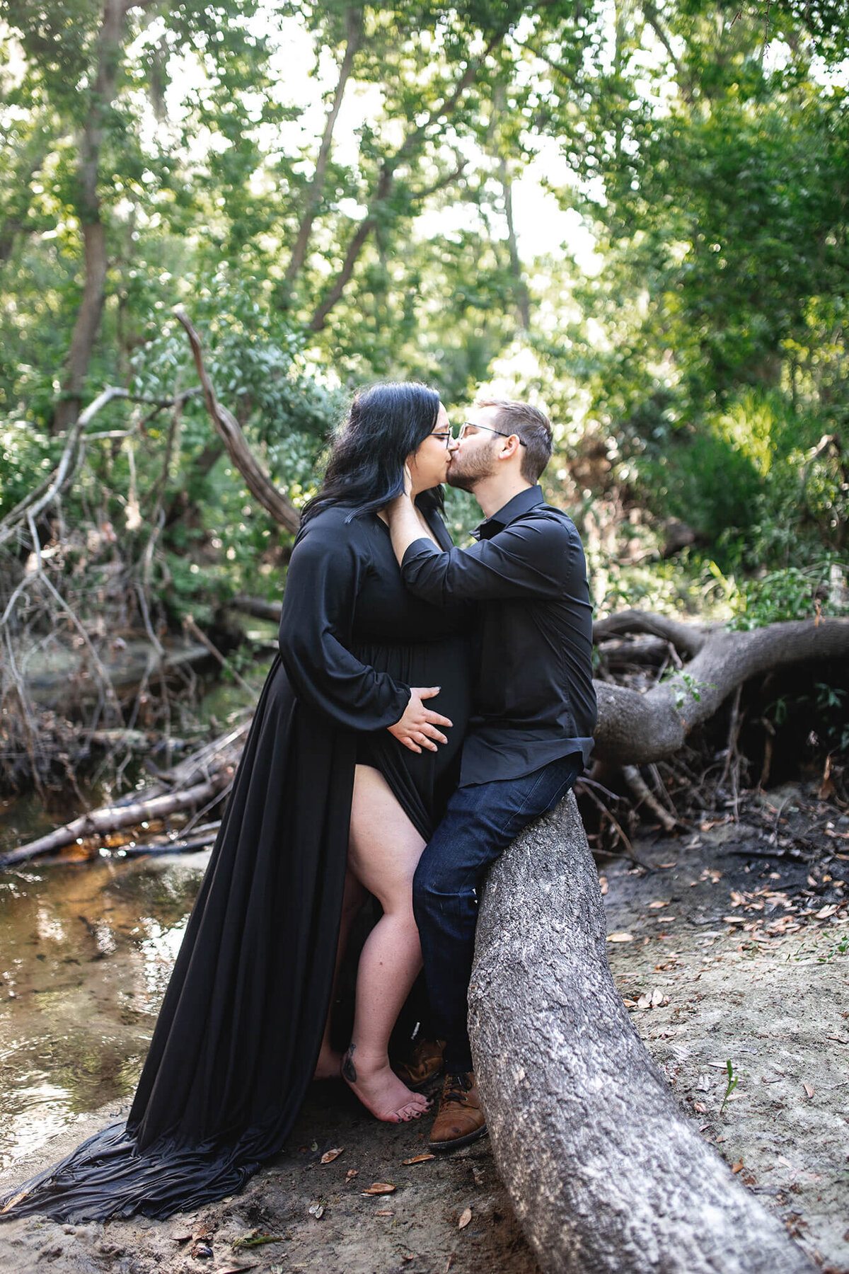 Intimate maternity session with expectant mother dressed in flowing black maternity gown while dad pulls her in for a kiss. Captured at Boyette Springs Park in Riverview, FL