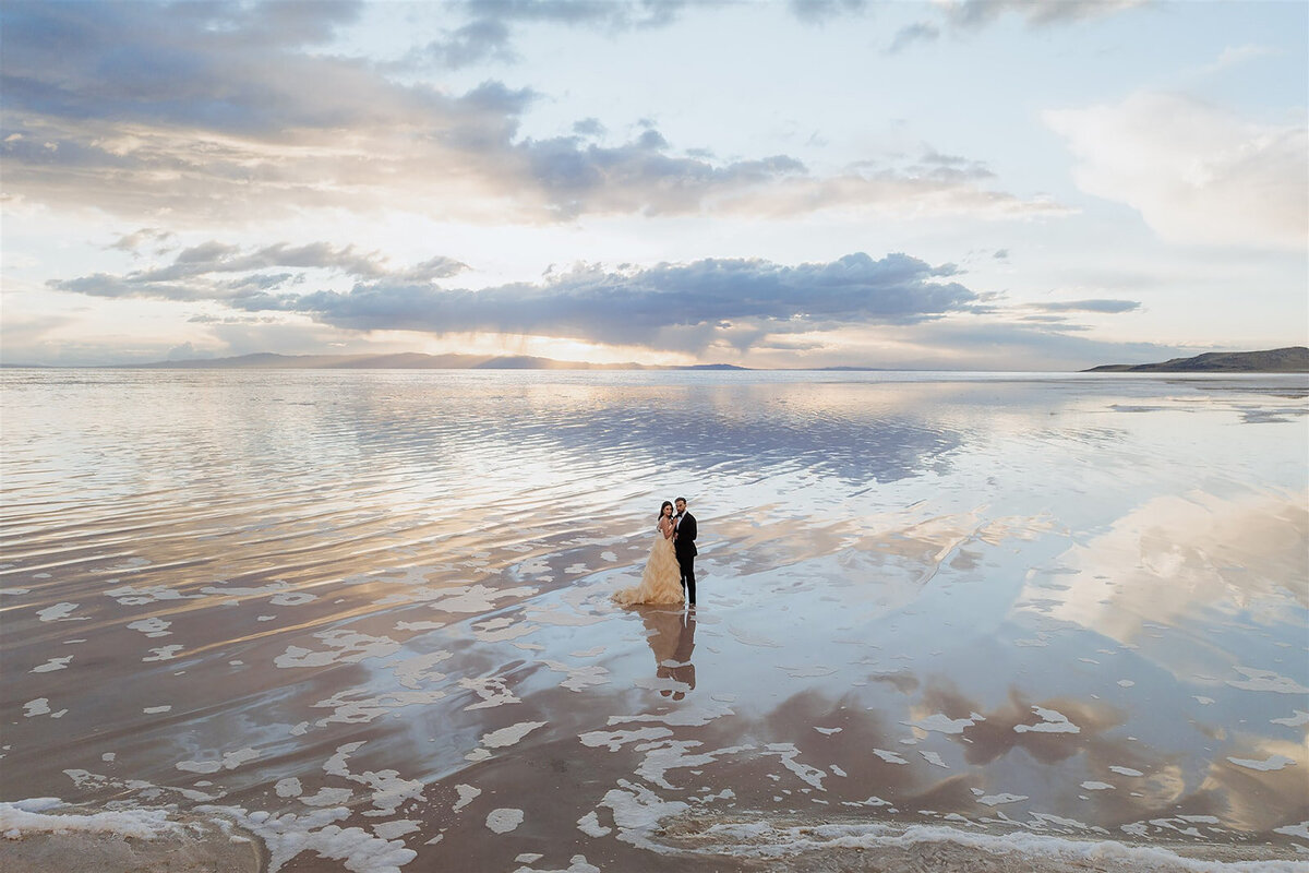drone image of bride and groom standing at the ocean shore