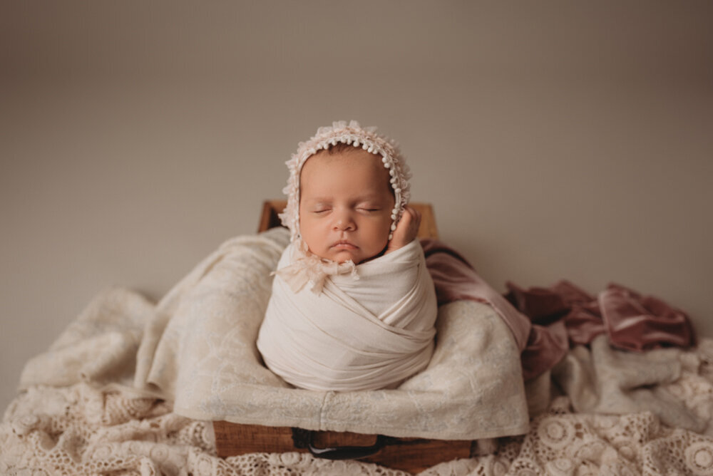 Newborn photo shoot photographed by Atlanta, Georgia newborn photographer with baby posing on neutral fabric with dainty headband on and sleeping with hands under chin.