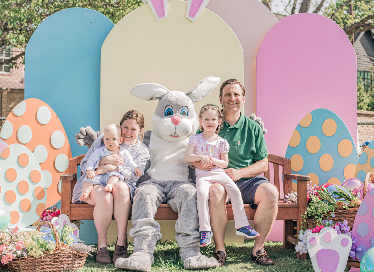 Family posing with Easter Bunny in front of a pastel colored Easter themed arch and egg shape backdrop