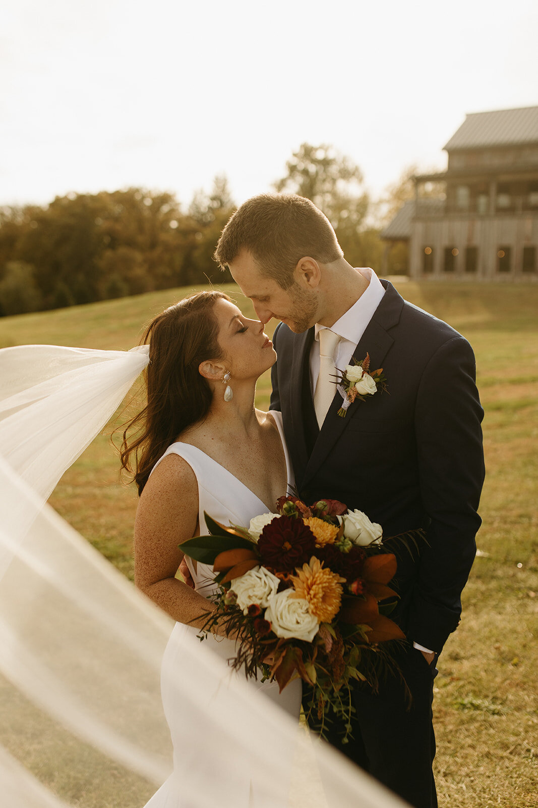 Bride and groom sharing a tender moment, with the bride holding a bouquet and the groom's suit complemented by a boutonniere, set against a sunset-lit field in Illinois.