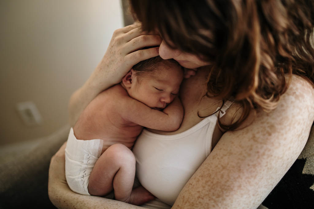 Mother snuggling tiny infant on her chest during lifestyle newborn photography session