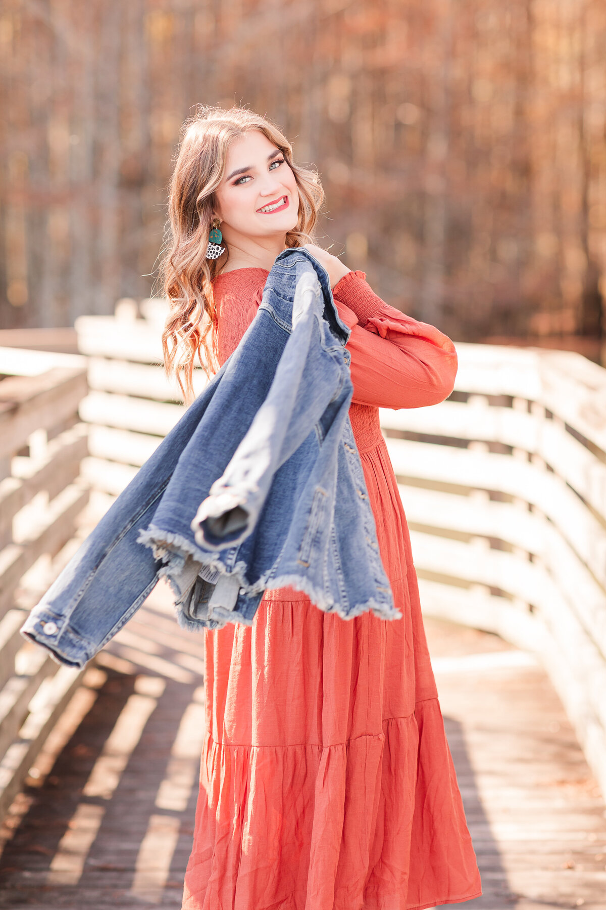 Senior girl in rustic orange dress with jean jacket on shoulder