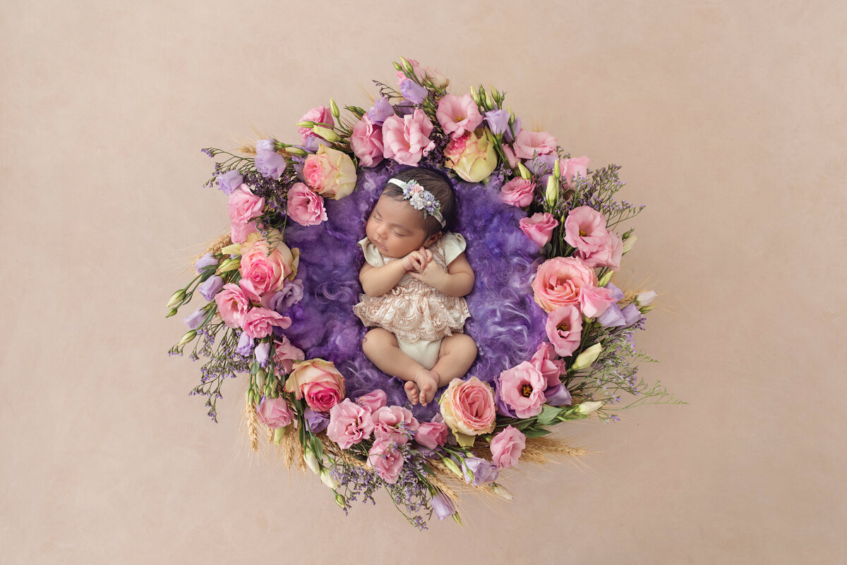 A newborn baby girl sleeps in the center of a colorful floral wreath for a NJ Newborn Photography session