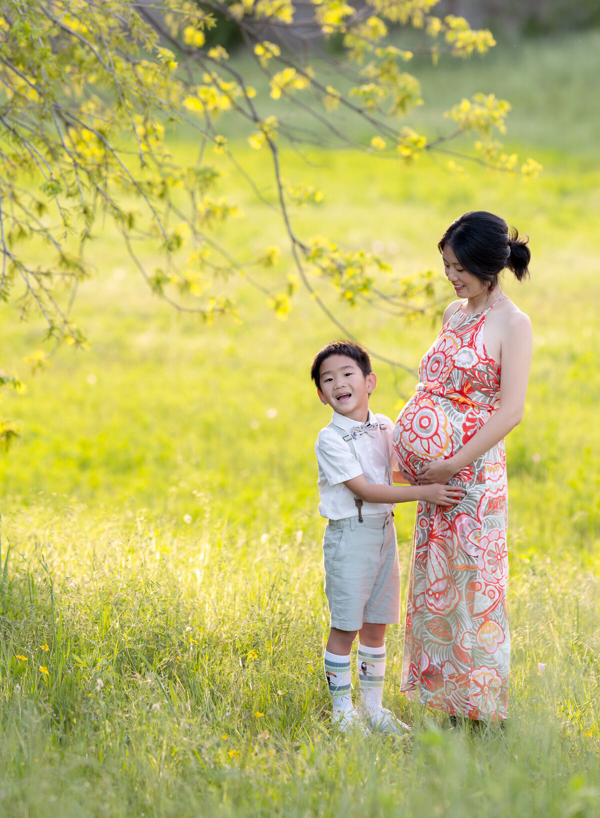 Joyful maternity photo of a mother and her young son laughing and holding her belly in a sunny Austin park.