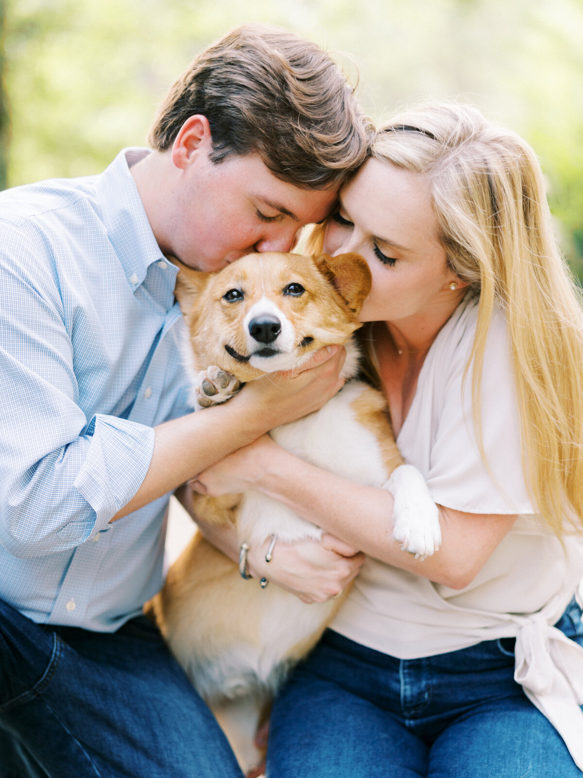 Man and woman in jeans holding and kissing their Corgi dog