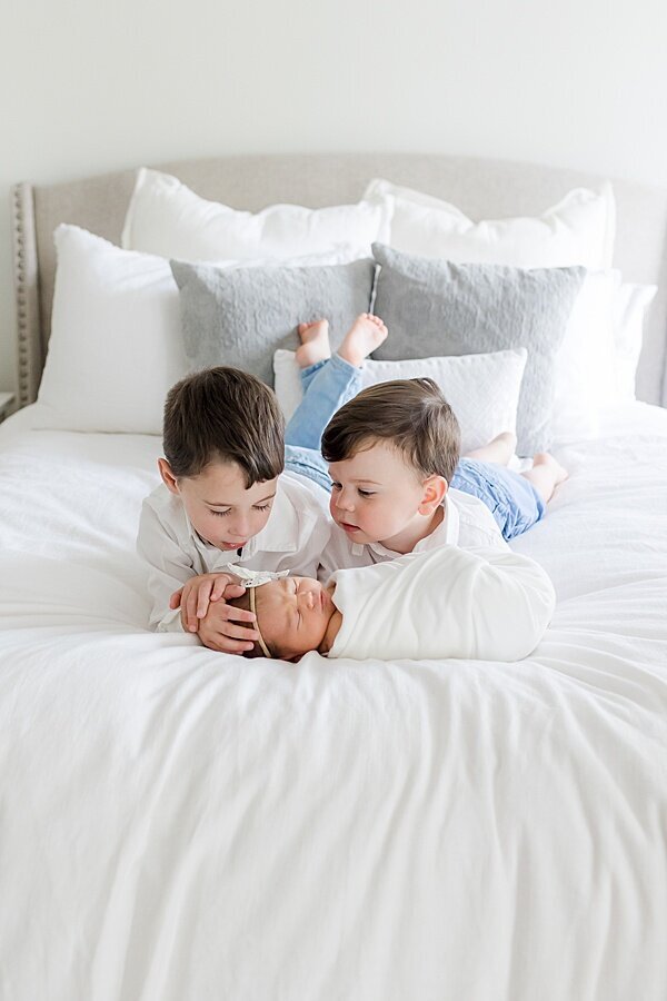 big brothers looking at little baby sister swaddled in white on bed by DC Newborn Photographer Emily