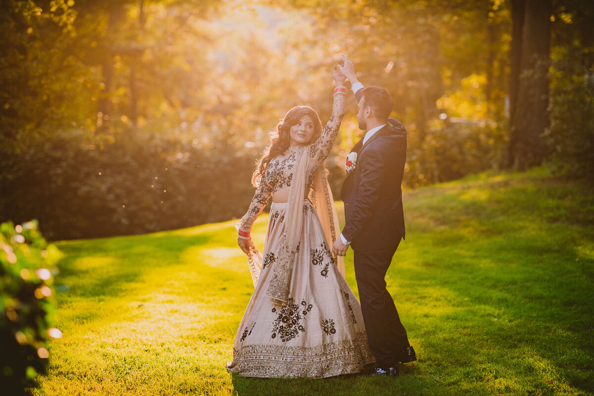 Groom twirling the bride during their indian wedding reception at the crest hollow country club at sunset