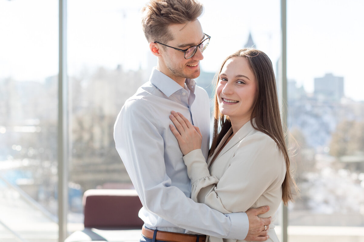 In a close-up portrait, Melissa and Yannick embrace with Parliament visible through the window, symbolizing their love against the backdrop of iconic landmarks.
