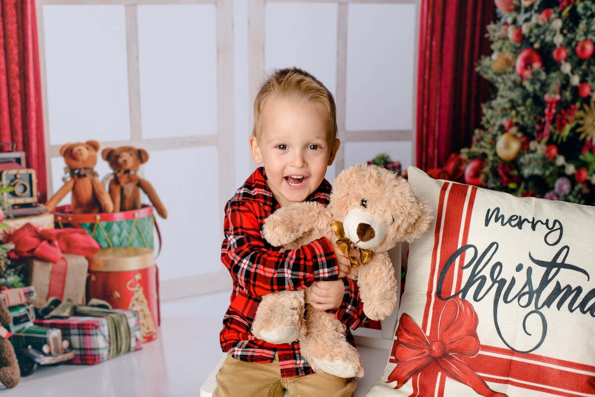 little boy dressed in plaid snuggles holiday teddy bear