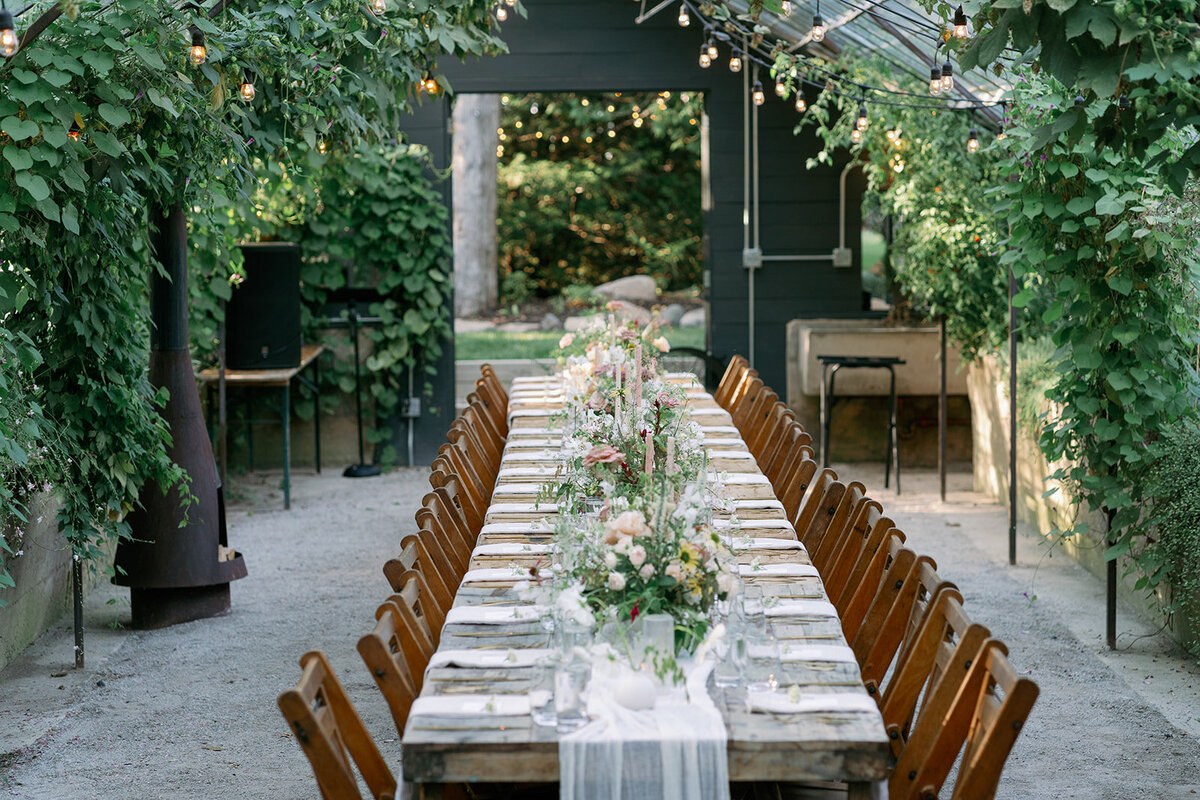Romantic candlelit wedding tablescape inside the Glasshouse Community greenhouse featuring florals, linens, and greenery.