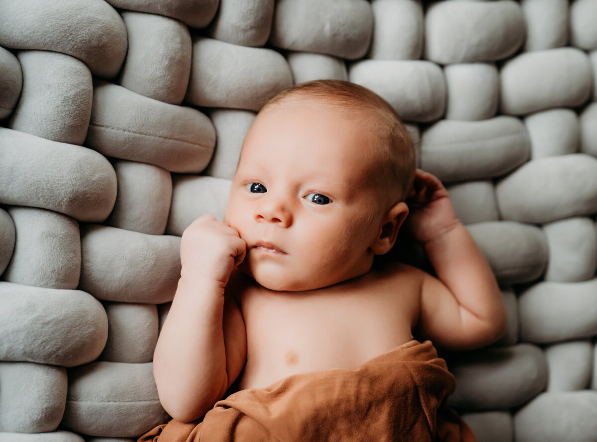 Newborn Photographer, a little baby is swaddled in blankets and lays  a comforter with large woven strands