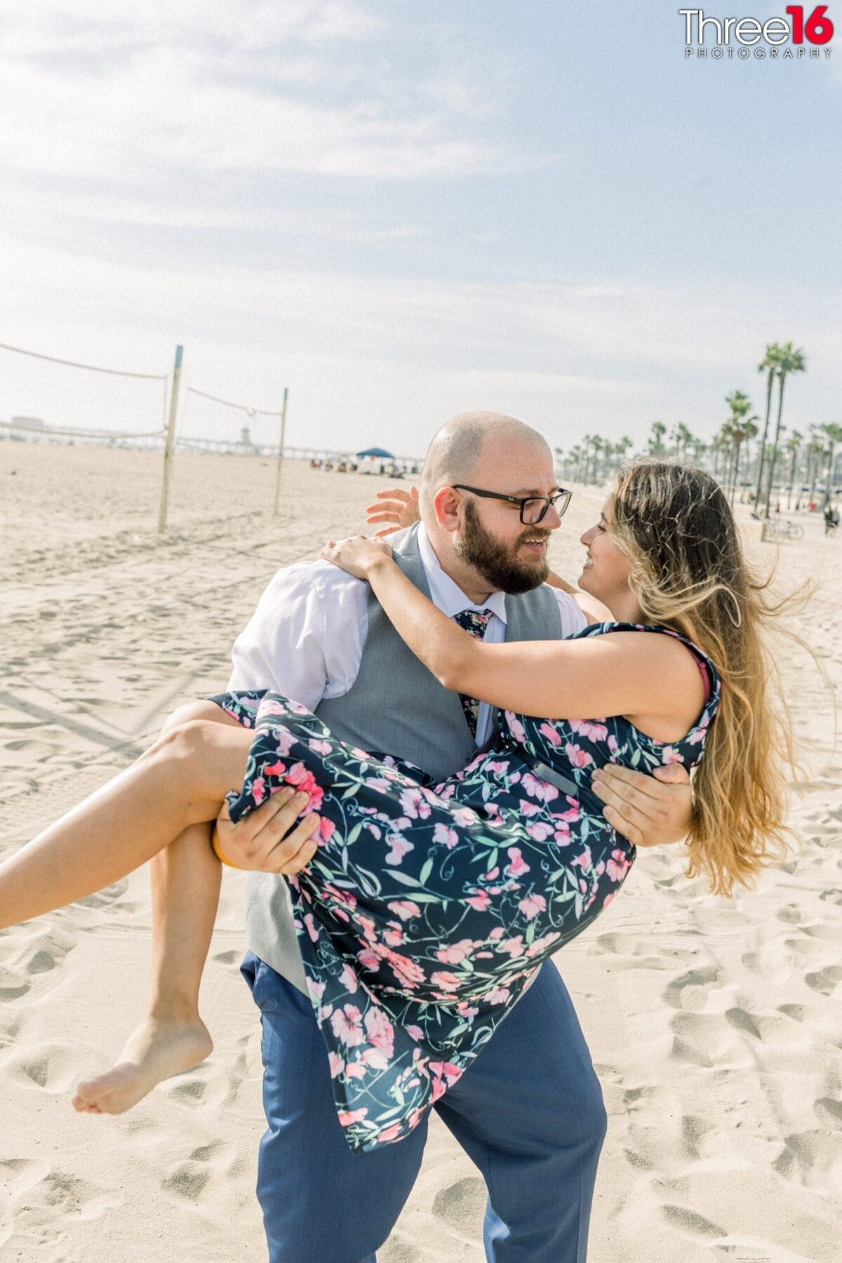 Engaged couple stare at each other as the Groom carries his Bride across the beach.