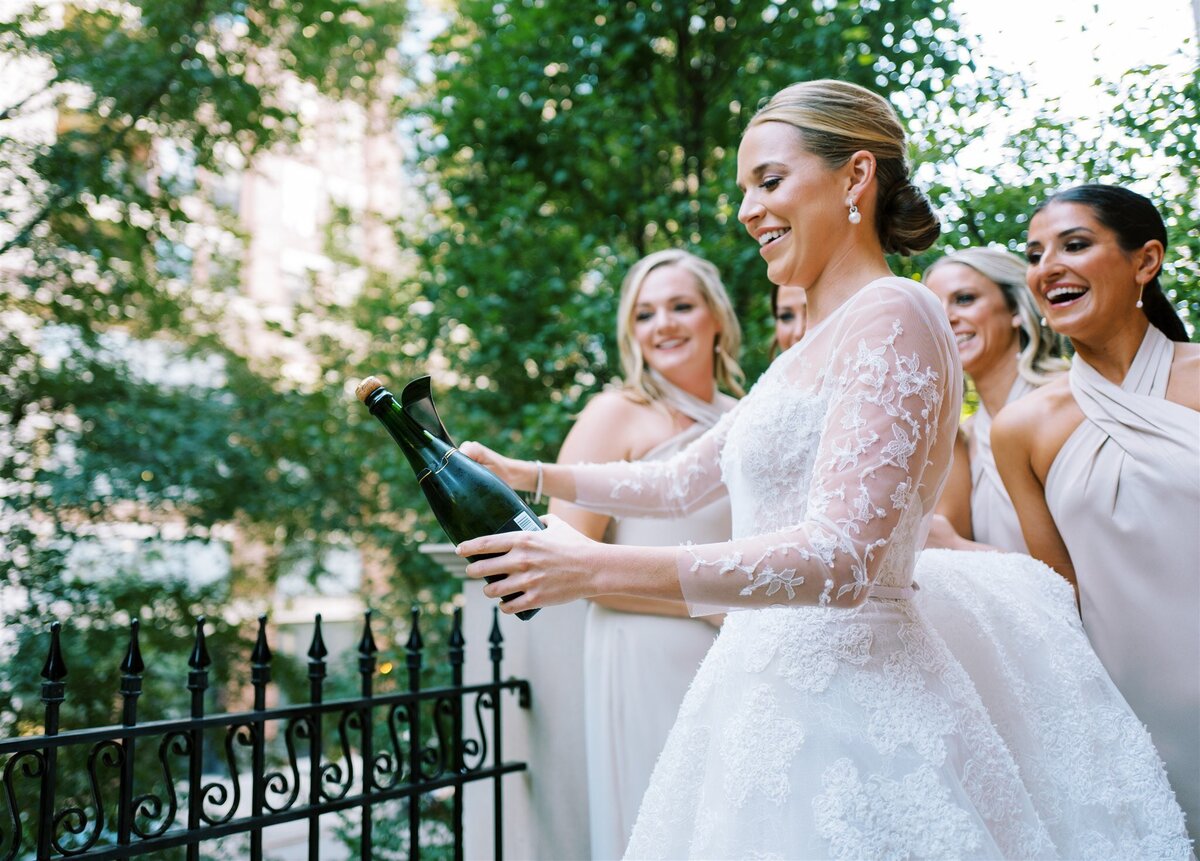 A photo of the bride slicing open a bottle of champagne with a knife.