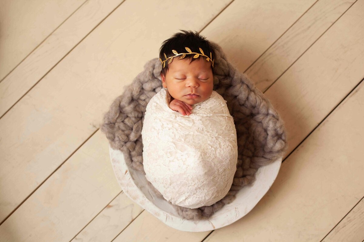 newborn girl in cream wooden bowl in cream wrap and headband