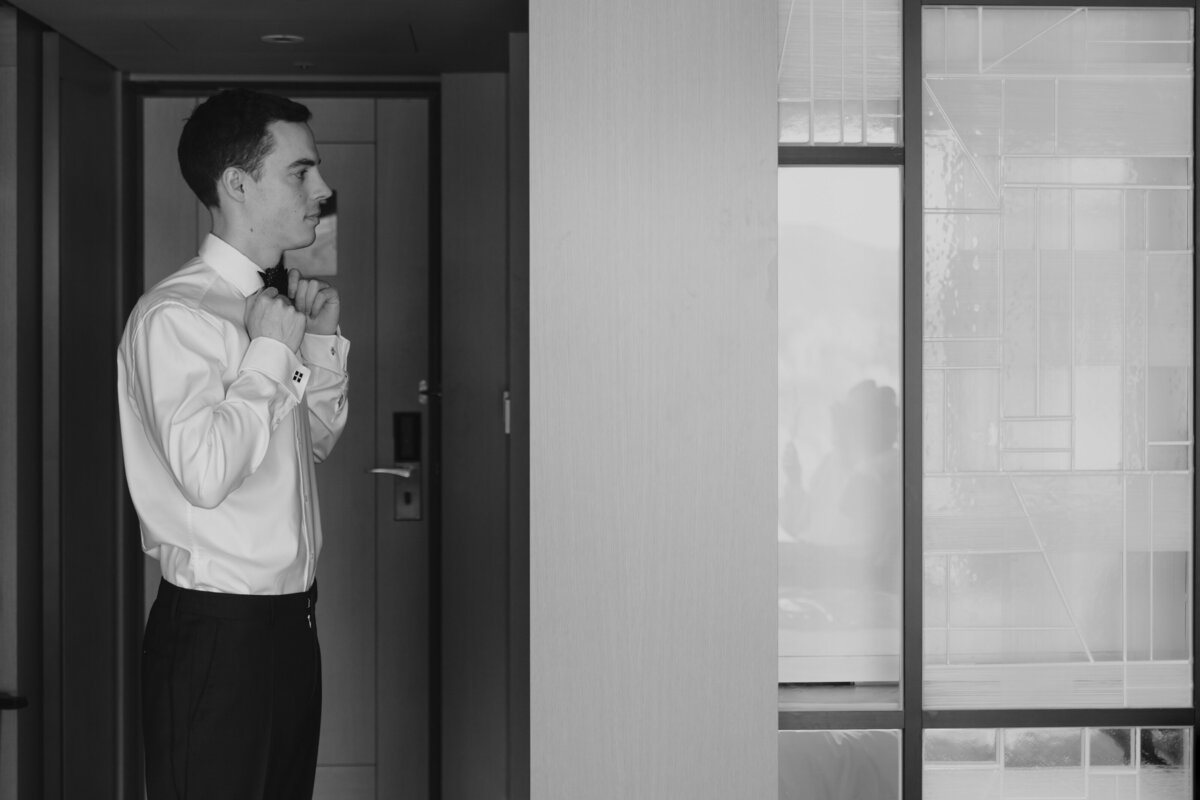 the groom fixing his bow tie in front of the mirror