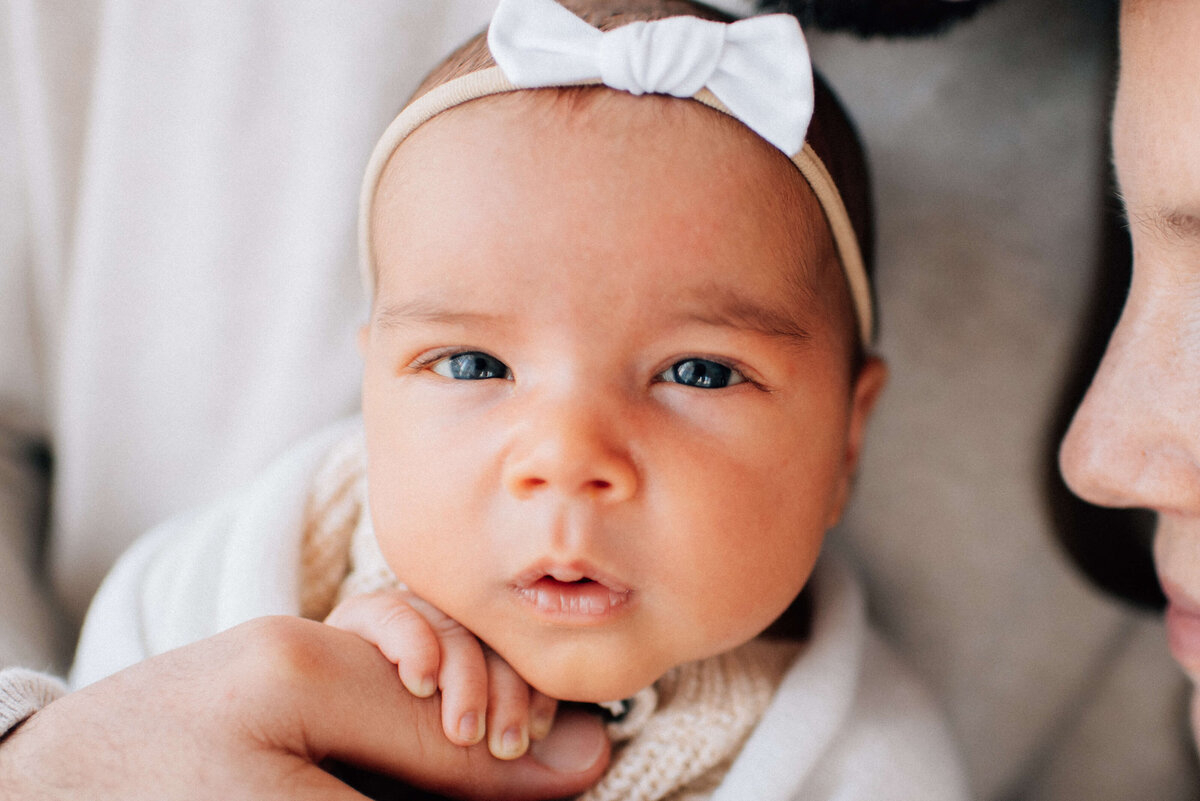 close up newborn face holding dad's thumb with her hand