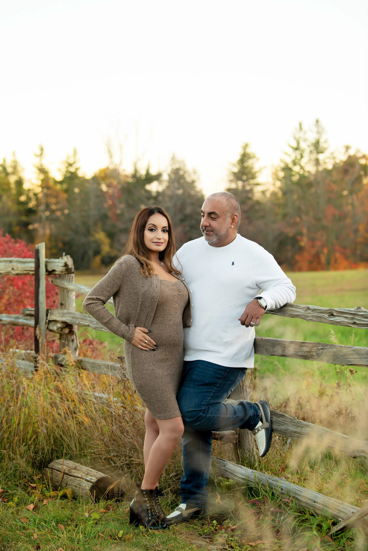husband and wife standing next to a wood fence for their outdoor fall maternity photos 