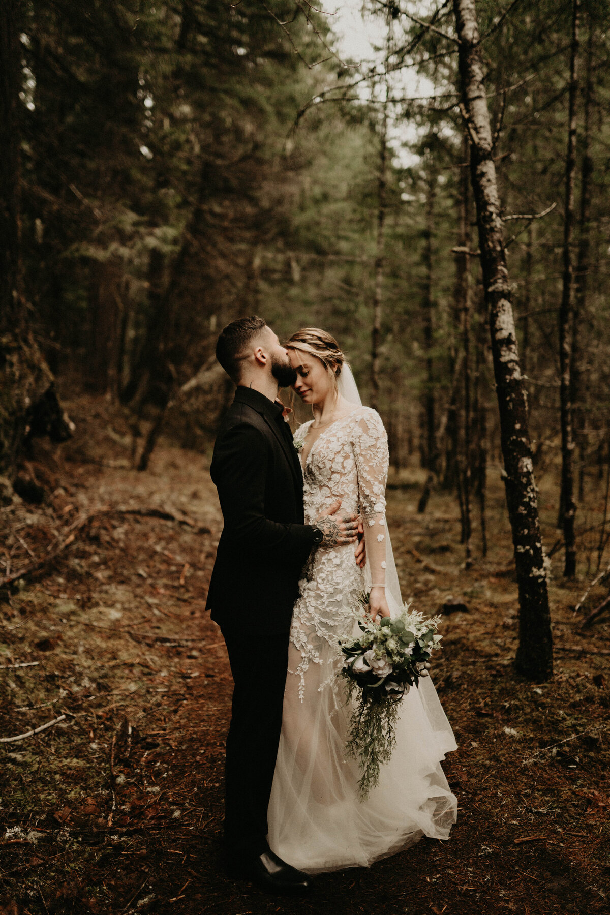 Groom kissing the forehead of bride in forest after elopement