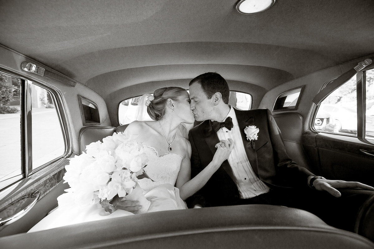 Newlyweds kissing in their vintage car.