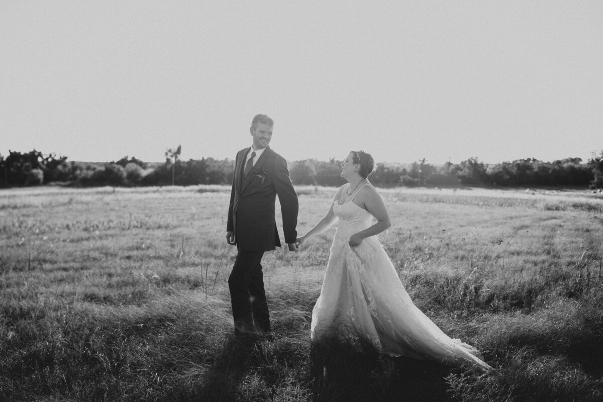 Bride and groom holding hands in an open field, captured in a black and white photo