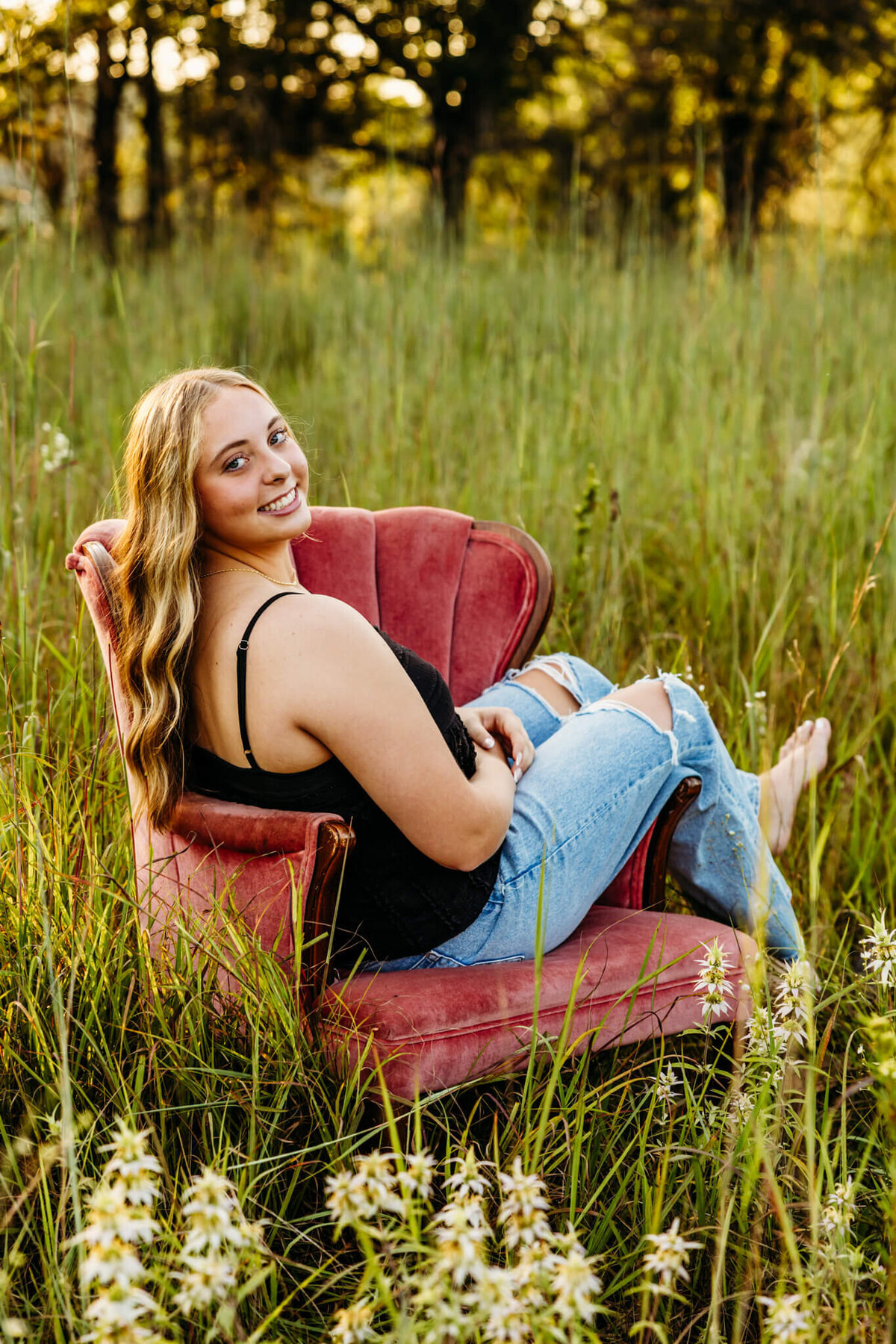 beautiful blonde teen girl in a black top and jeans sitting on a vintage chair in a flower field near Green Bay. 
