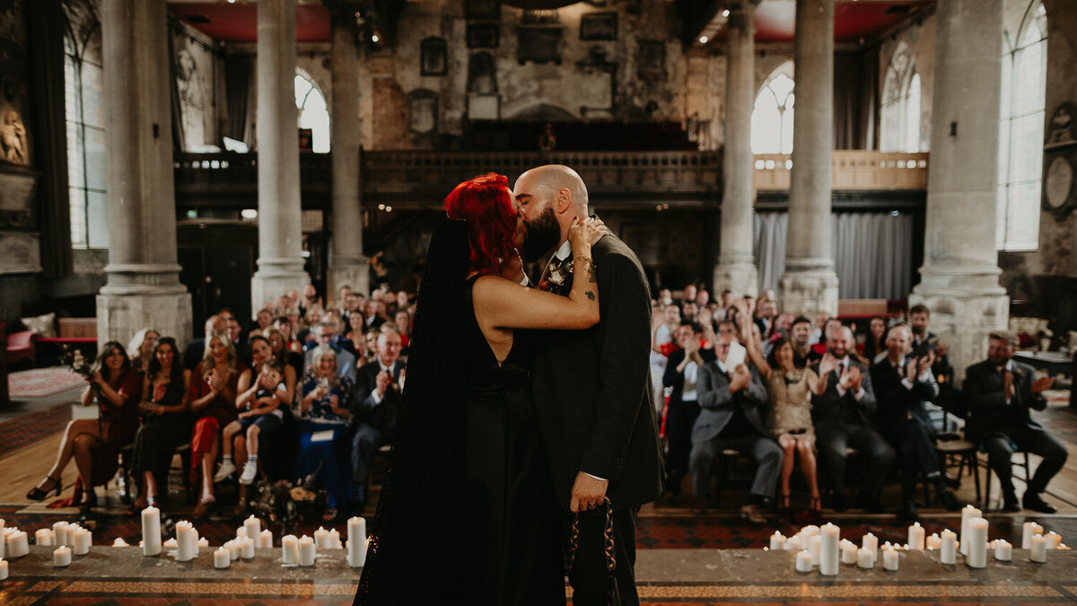 Bride wearing a black dress kisses her groom in front of all their family and friends at The Mount Without in Bristol. 