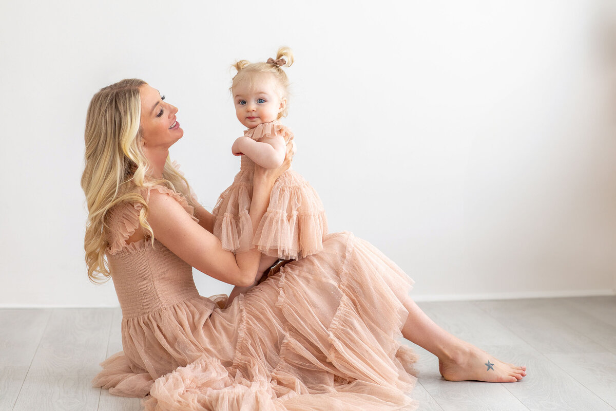 A mom sits with her toddler in her lap, lovingly looking at her child as the toddler gazes at the camera during a tender family moment
