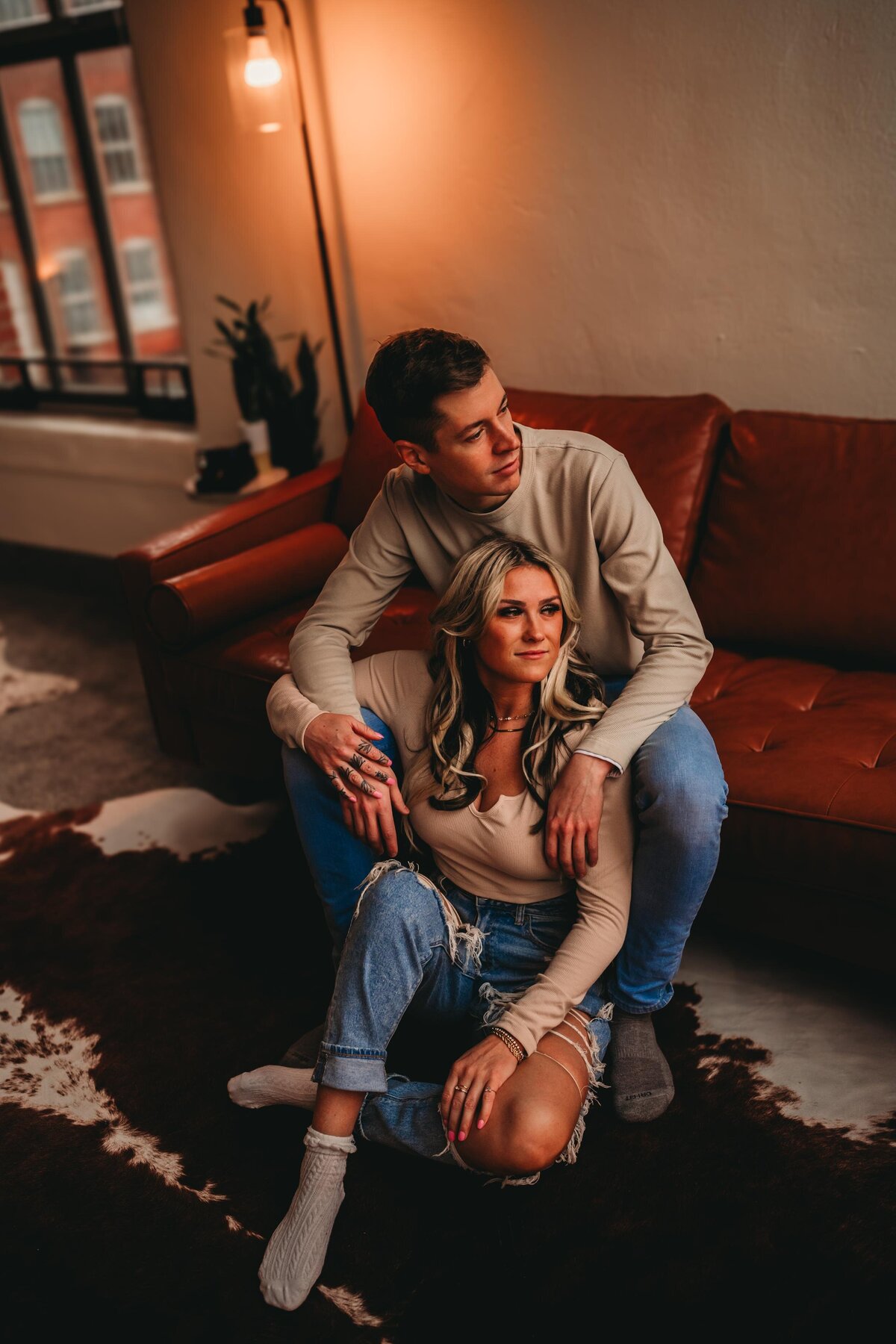 Romantic couple’s indoor session on a leather couch with warm lighting, showcasing cozy, editorial-style photography in Pittsburgh.