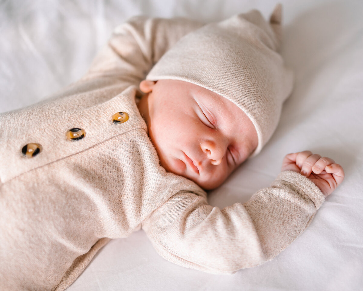 Newborn baby sleeping on a white blanket. His eyes are closed and he is dressed with a beige cap and outfitNewborn baby sleeping on a white blanket. His eyes are closed and he is dressed with a beige cap and outfit