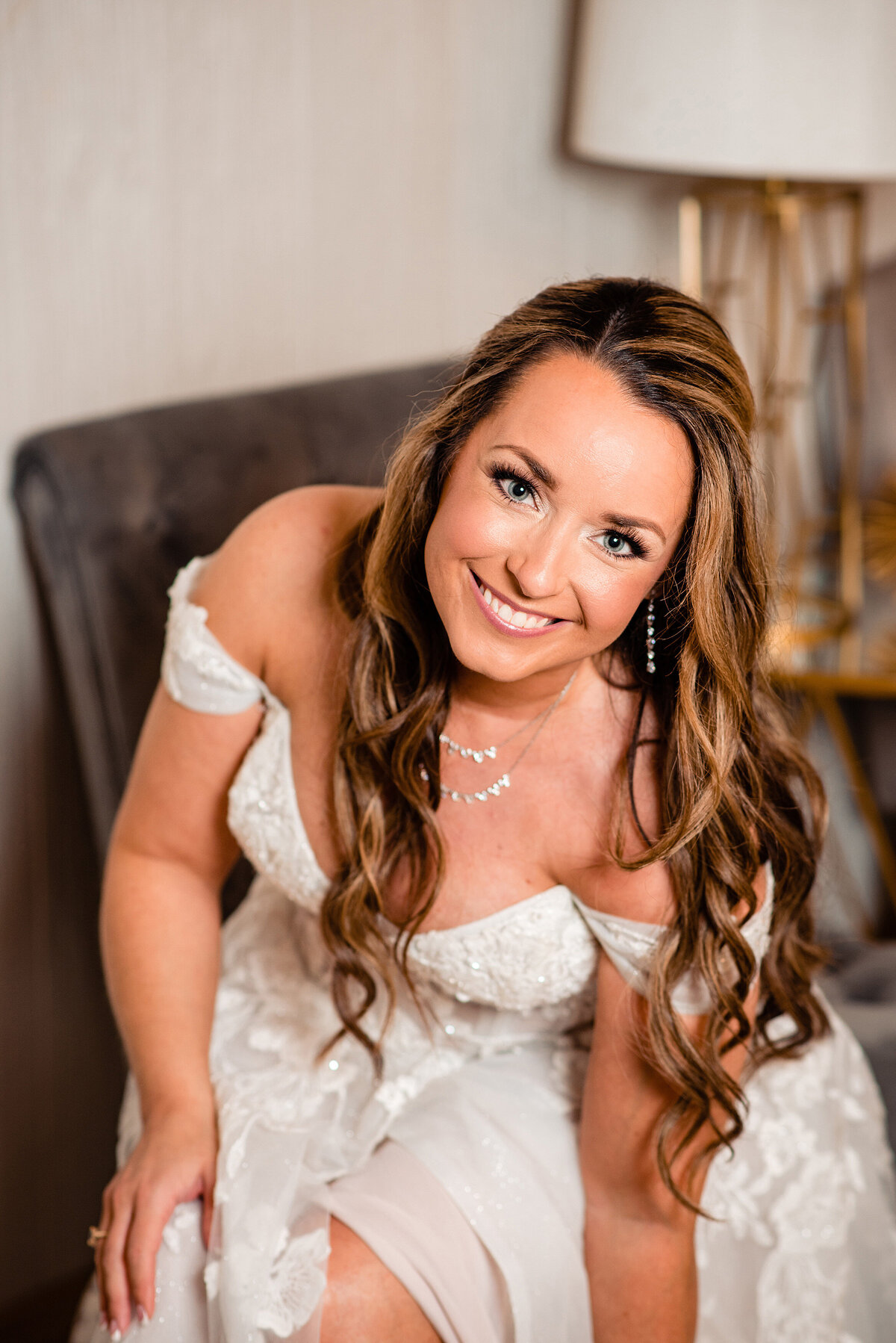 Bride smiling up at the camera while putting on her wedding shoes