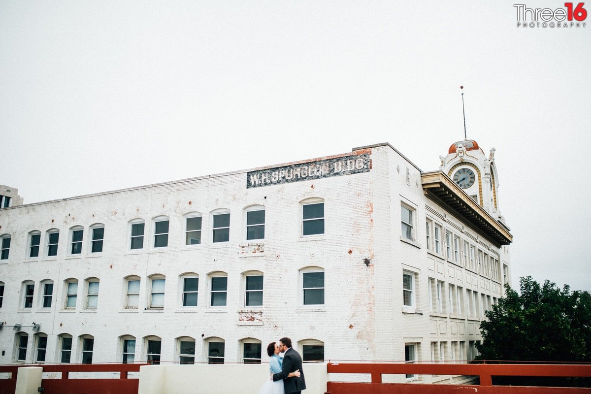 Engaged couple share a kiss with a Santa Ana historic building in the background