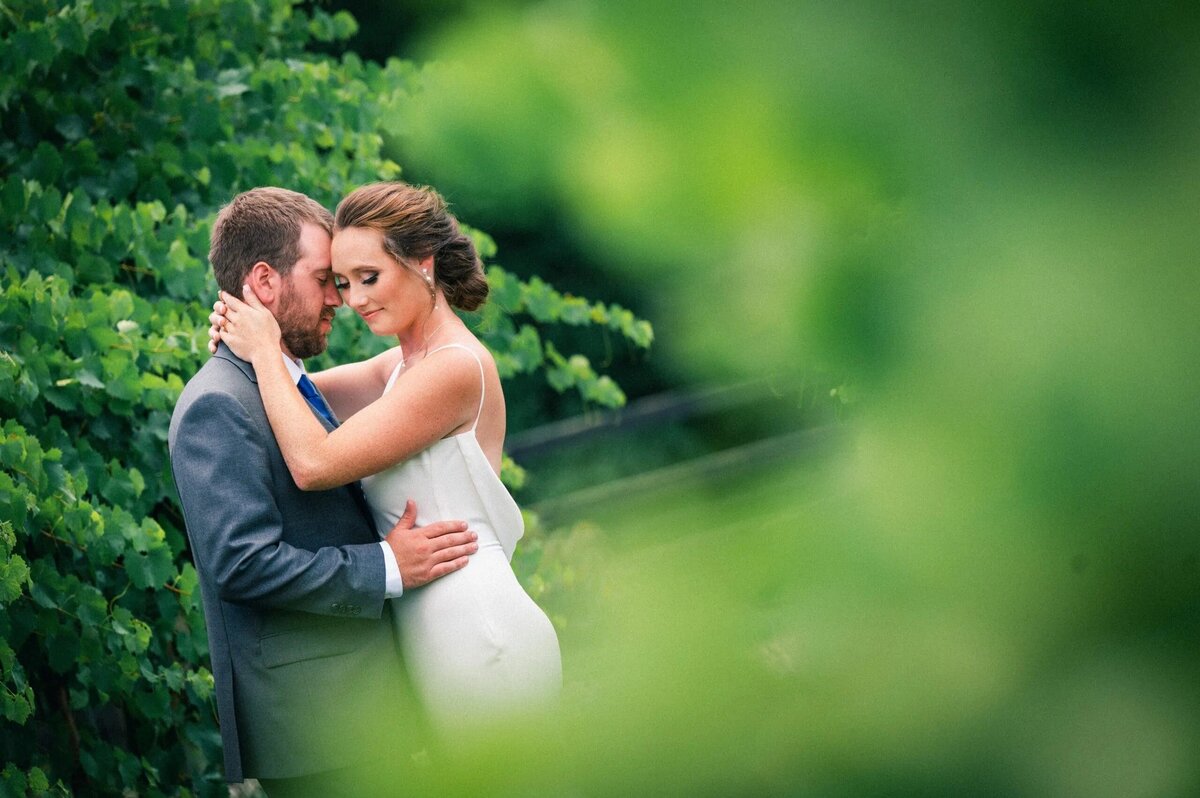 A wedding couple in a close embrace surrounded by greenery.