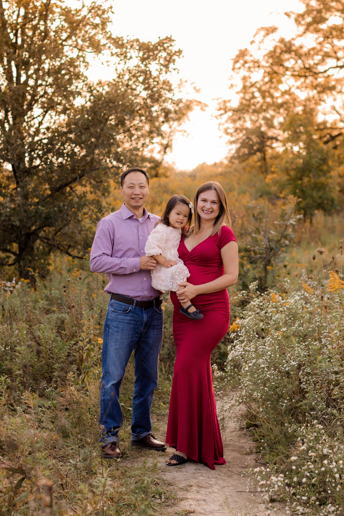 A glowing pregnant mom portrait with her family in a field of flowers.