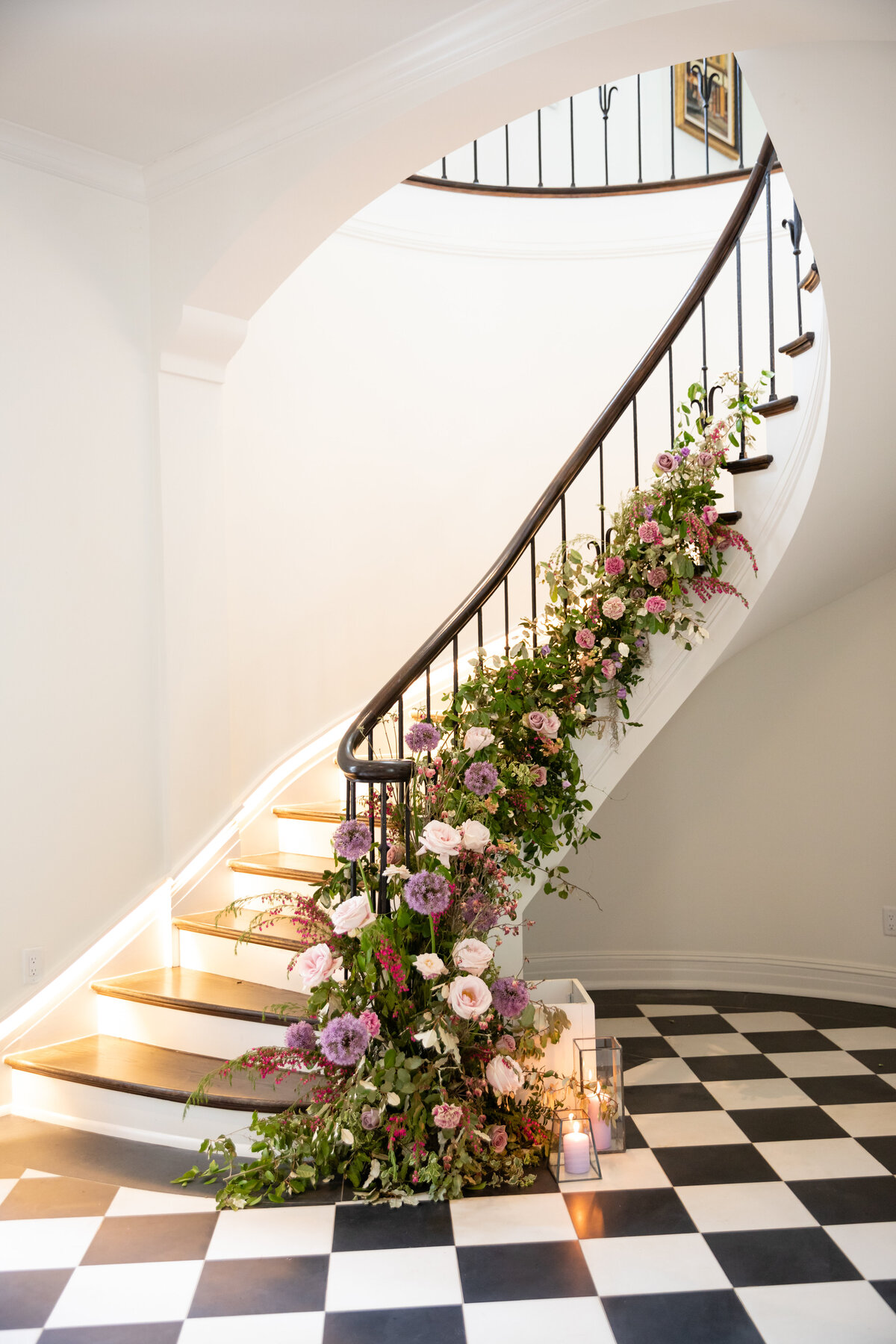 Lush floral installation growing up the staircase with natural greenery, purple globe allium, blush garden roses, and pastel wildflowers. Bridgerton inspired engagement party at a private home in Nashville, TN.