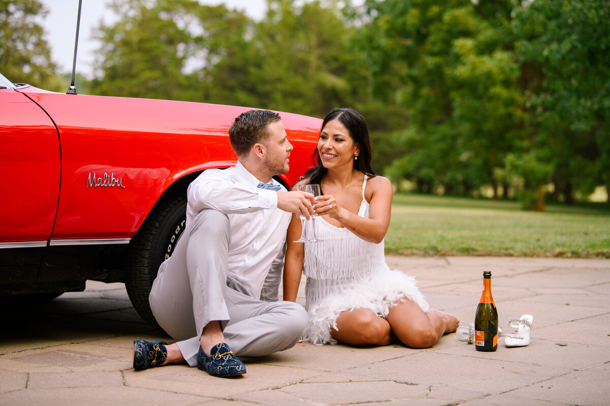 Couple sitting by car drinking champagne