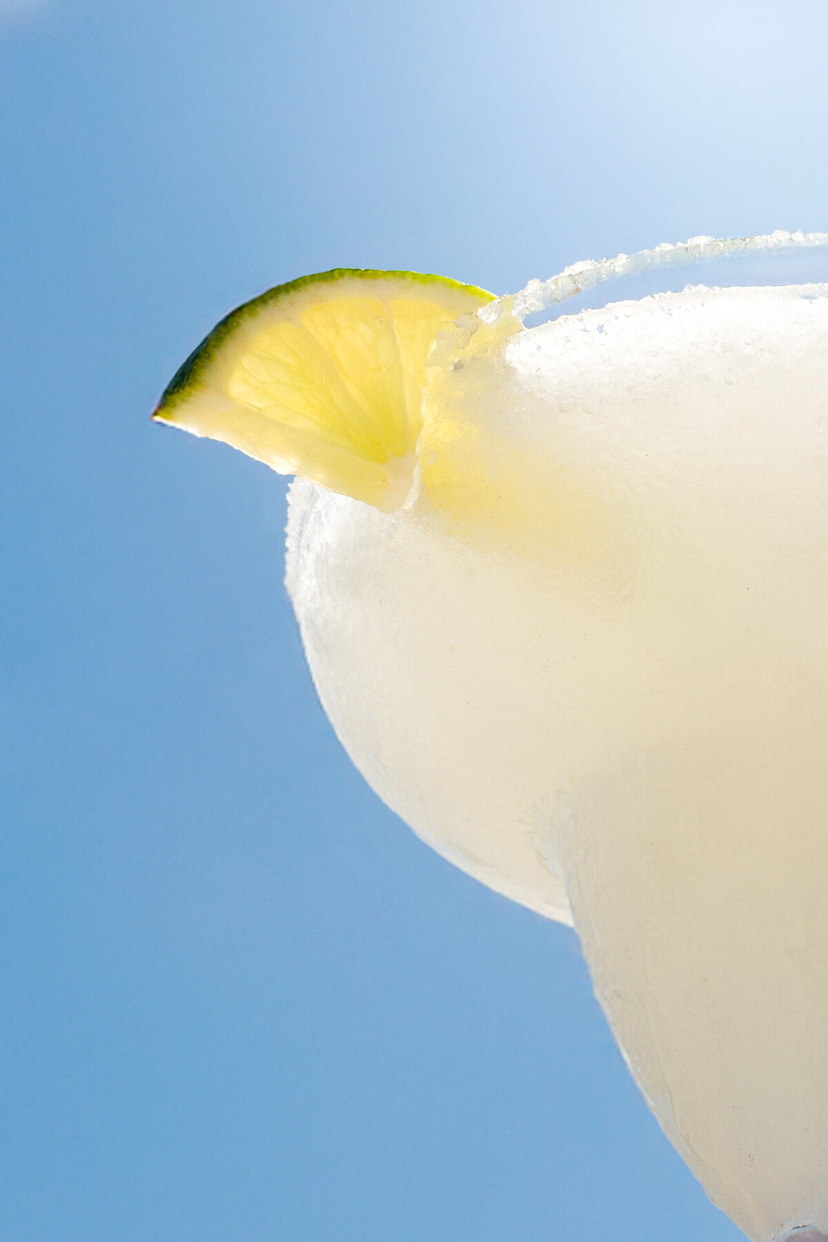 a frozen margarita with a lime wedge and salted rim on a bright sunny day.