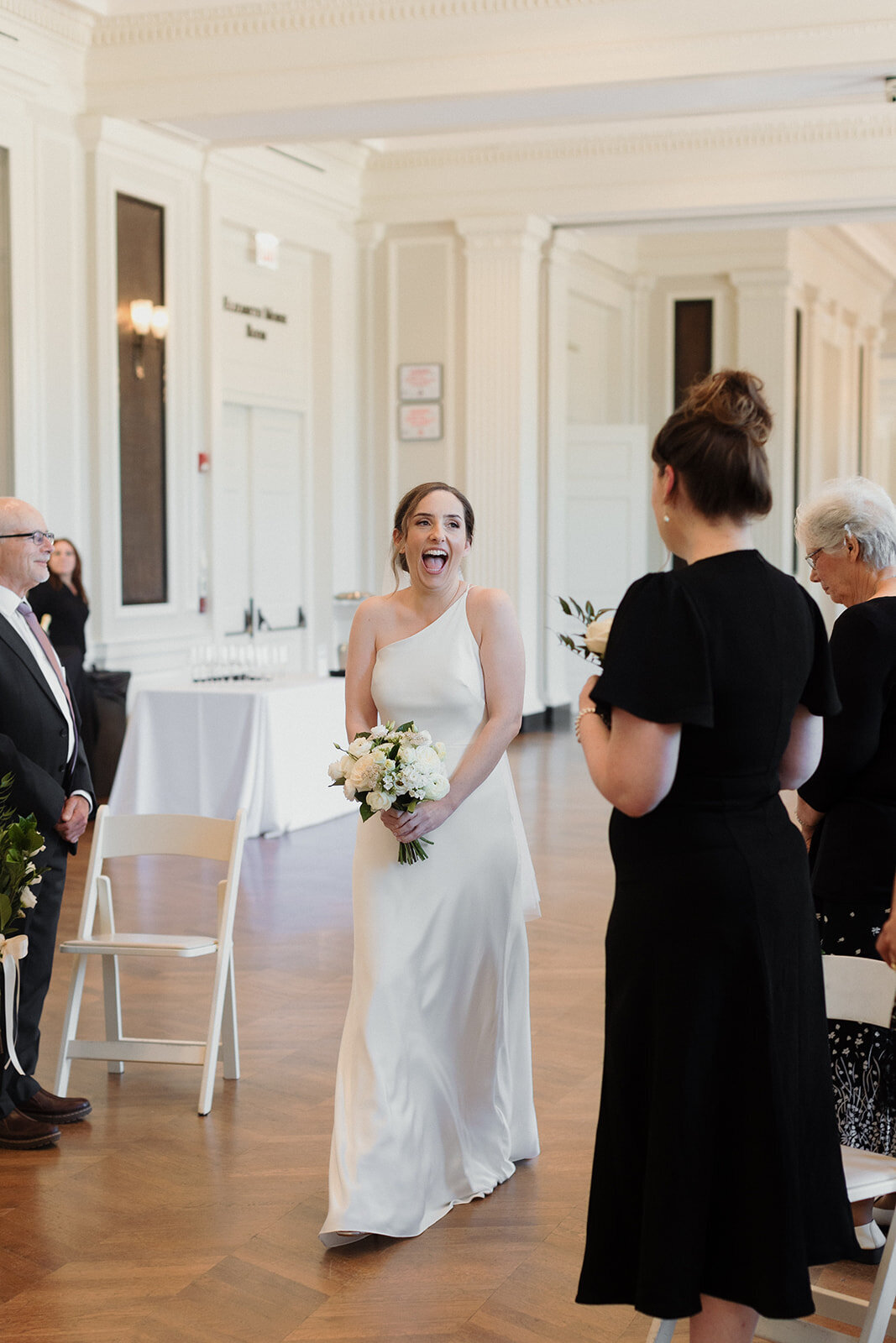 joyful bride walking down the aisle and smiling at her friend, she carries a small bouquet