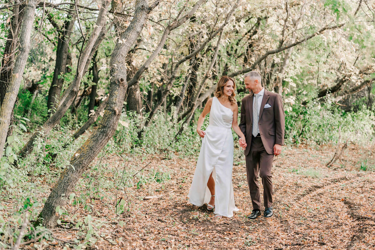 Bride and groom walking together under a canopy of  fall trees.