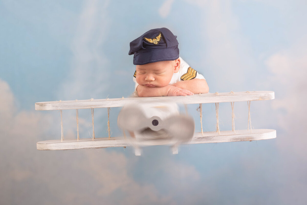 Newborn dressed as a pilot with a vintage airplane prop, captured in Overland Park, Kansas. A delightful setup for families seeking adventurous and themed newborn photography in the Kansas City metro area
