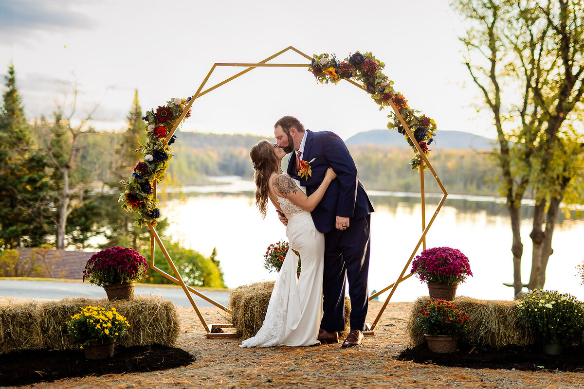 groom kissing bride in front of arbor at white mountain wedding in Lancaster NH