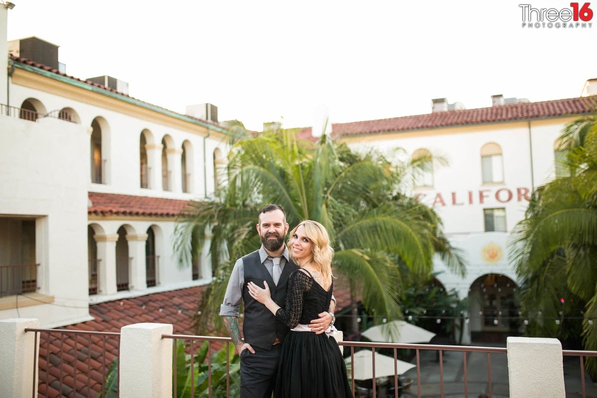 Engaged couple embrace as they stand on the second floor overlooking the Villa Del Sol