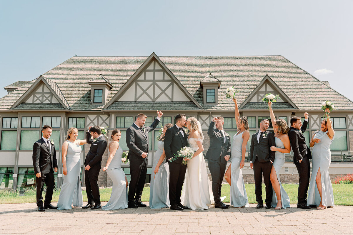 bride, groom, bridesmaids and groomsmen all standing side by side in front of a large white house