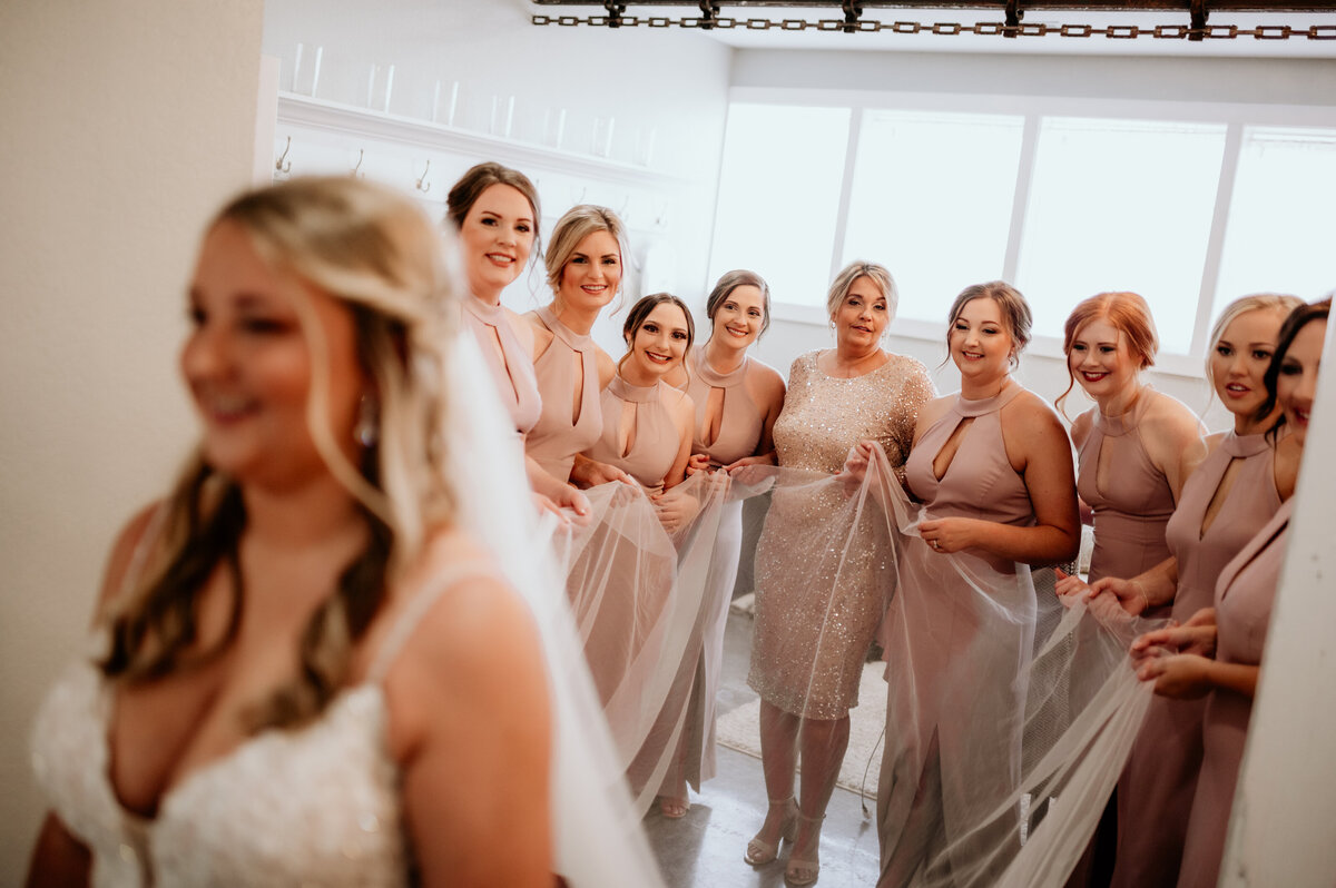 bridesmaids standing behind the bride and holding her veil together